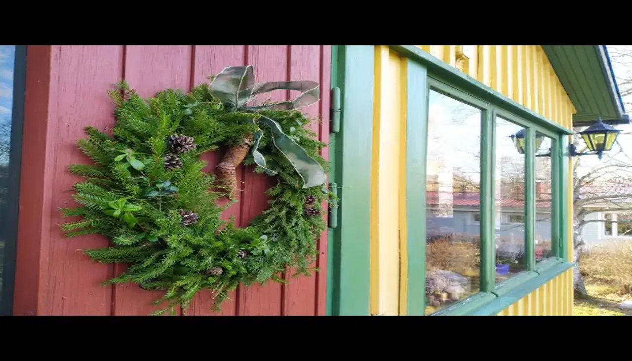 Vacker julkrans med kottar och grönt band, redo att binda julstämning på en röd dörr.