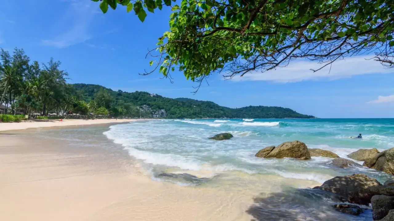 Piękna plaża Kata Beach z turkusową wodą, falami i zielonymi wzgórzami w tle. Idealne miejsce na relaks.