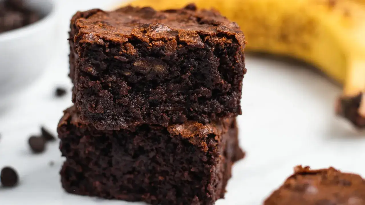 Dwa pyszne brownie bananowe ułożone jedno na drugim, z bananem w tle i kilkoma kawałkami czekolady.