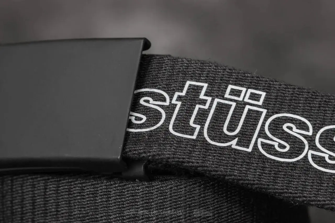 Cintura Stüssy nera con fibbia metallica. Il logo Stüssy bianco è ben visibile sul tessuto.