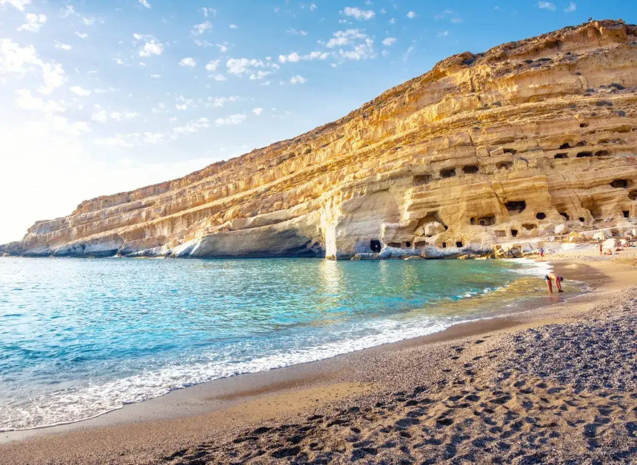 Matala, Kreta: Ein sonniger Strand mit Höhlen in den Felsen, einst ein Hippie-Dorf. Türkises Wasser und goldene Klippen.