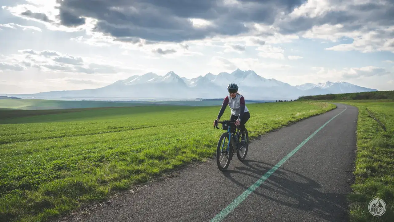 Kobieta na rowerze przemierza malowniczą trasę z widokiem na ośnieżone Tatry. To idealne miejsce na velo tatry.