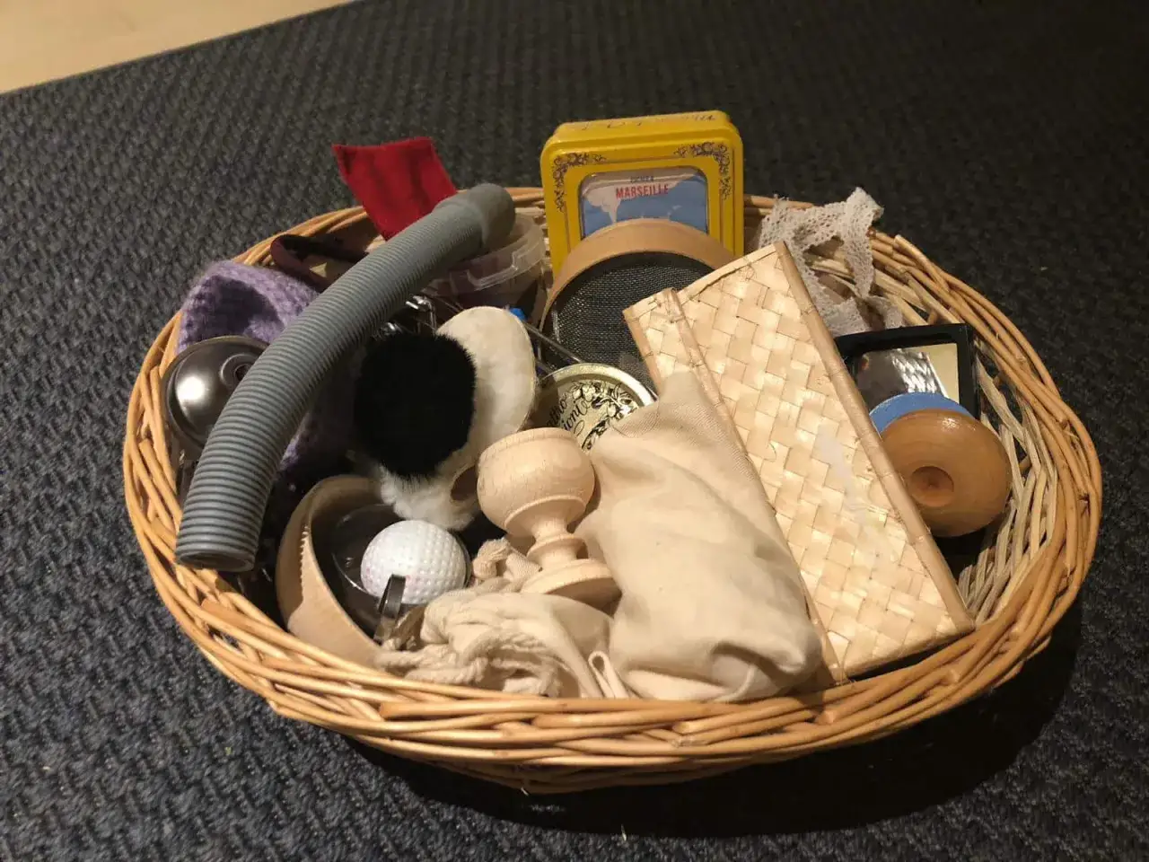 Un cestino dei tesori pieno di oggetti curiosi: un tubo grigio, una pallina da golf, un piccolo specchio, un contenitore giallo e altri elementi da esplorare.