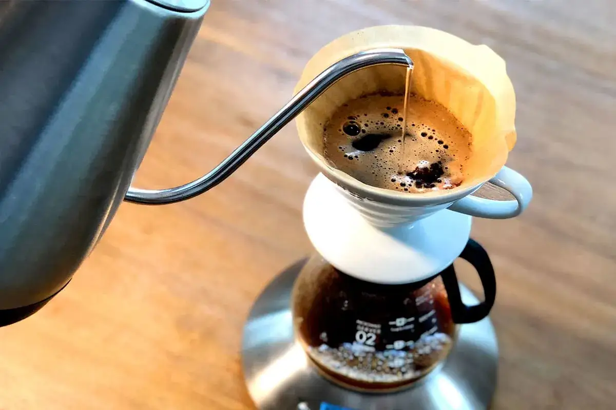 Precyzyjne parzenie kawy metodą v60 drip. Gorąca woda powoli przelewa się przez zmielone ziarna, tworząc aromatyczny napar.