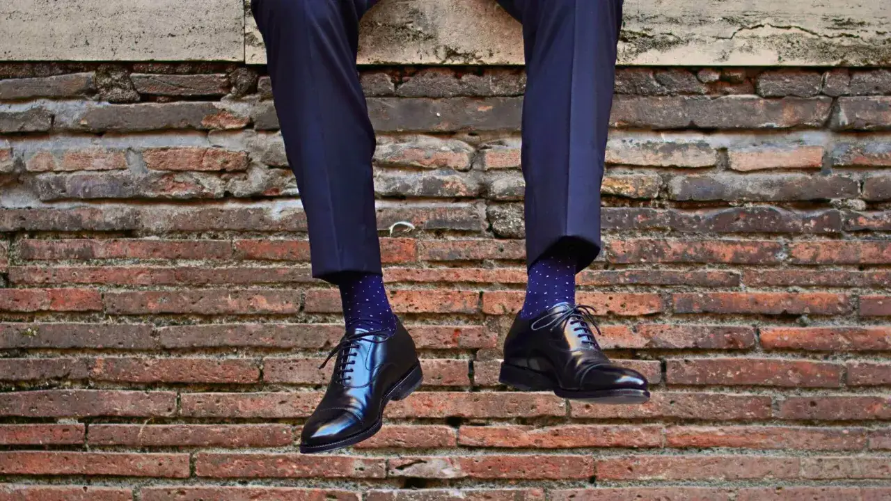 Un uomo con pantaloni blu scuro e calzini a pois blu abbinati a eleganti scarpe stringate nere.