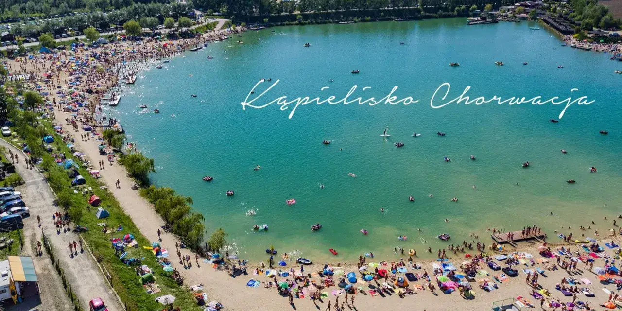Tłoczna plaża i turkusowa woda na kąpielisku Mała Chorwacja. Ludzie opalają się, pływają i relaksują na dmuchanych materacach.
