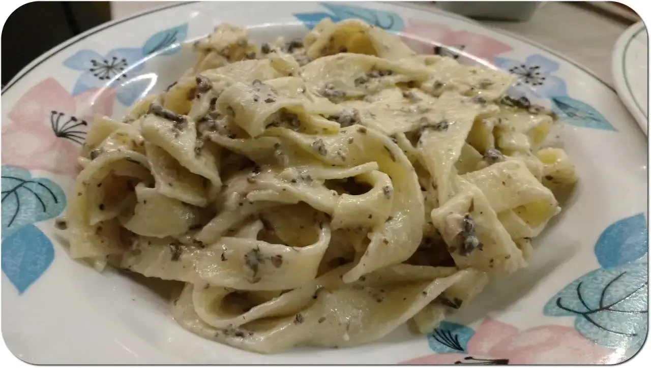 Pappardelle w kremowym sosie truflowym, ozdobione delikatnymi kwiatami na talerzu. Pyszne danie, które rozpływa się w ustach.