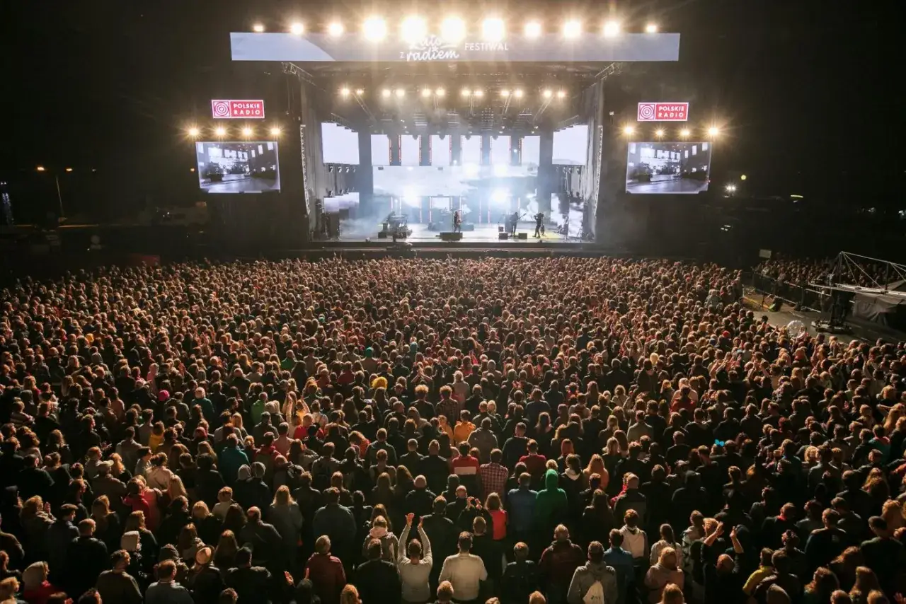 Tłumy ludzi na koncercie festiwalowym w Polsce. Na scenie zespół, a nad nim logo Polskiego Radia.