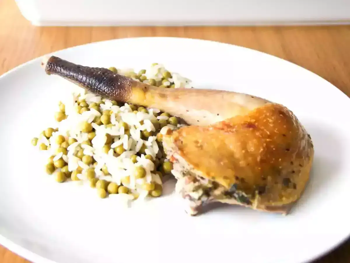 Une cuisse de pintade dorée, servie sur un lit de riz et de petits pois. Un plat savoureux et bien présenté.