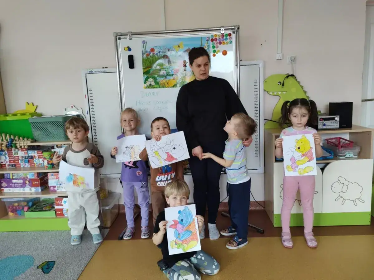 Dzieci w przedszkolu świętują dzień książki, prezentując swoje rysunki z Kubusiem Puchatkiem.