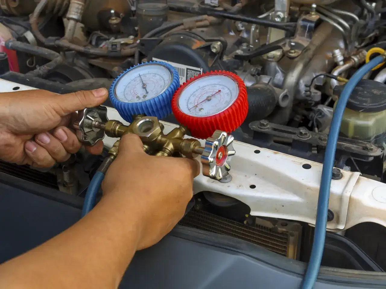 Hands connect gauges for an AC pump replacement, checking pressure under the car's hood.