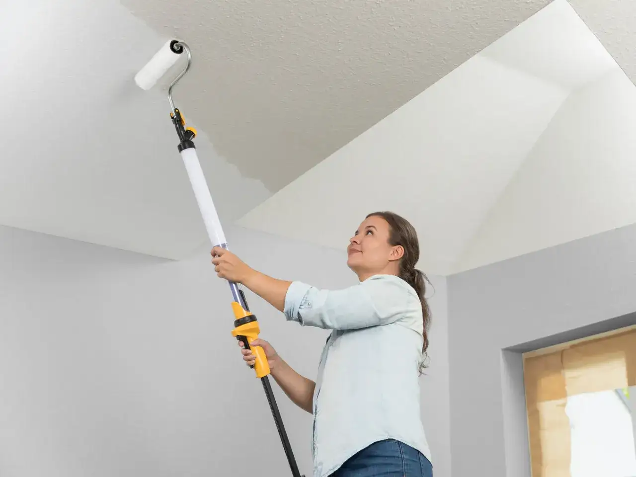 Donna imbianca il soffitto con un rullo estensibile, un modo semplice per imbiancare soffitto senza fatica.