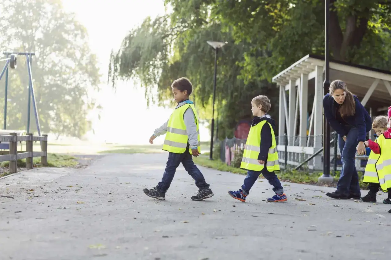 Des enfants en gilets fluo traversent la rue, accompagnés d'une adulte. Une scène illustrant la réglementation du déplacement à pied ACM.