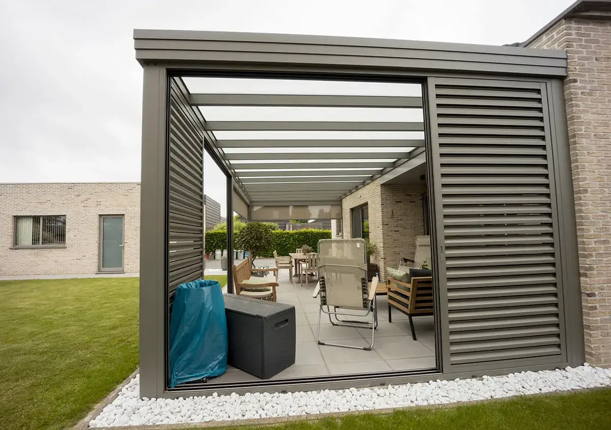 Une pergola moderne transformée en véranda, avec mobilier de jardin et vue sur une pelouse.