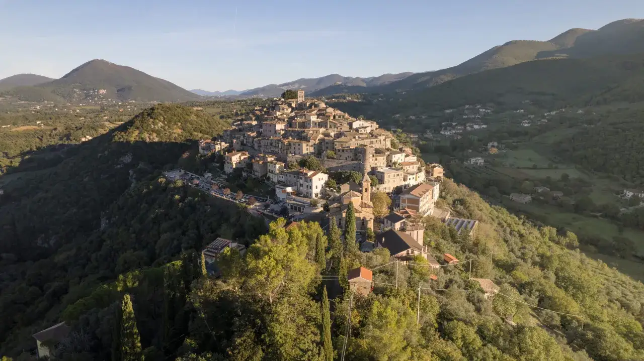Borgo arroccato sui monti Sabini, con case in pietra e tetti rossi, immerso nel verde della campagna laziale.