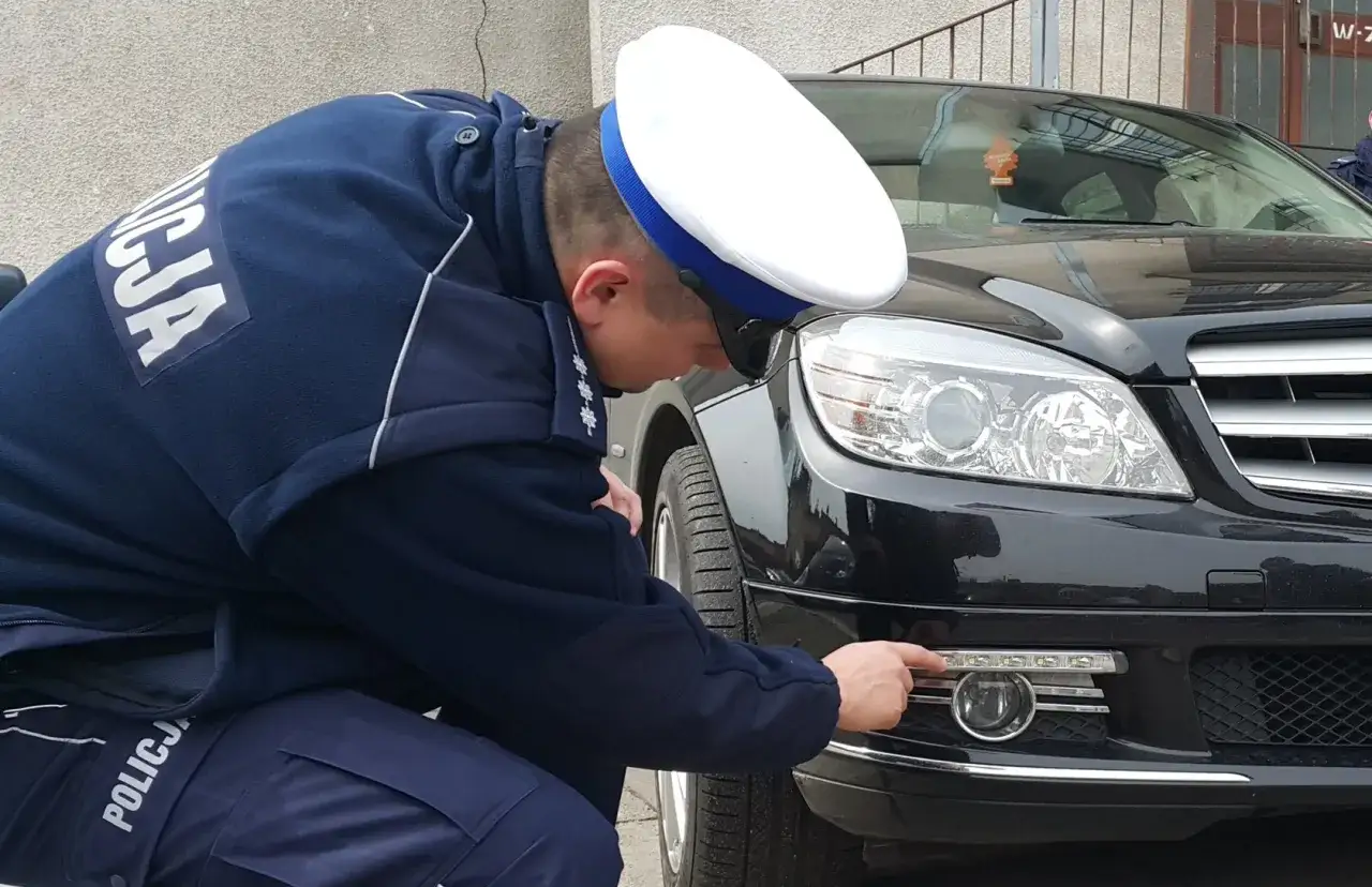 Policjant sprawdza, jakie światła do jazdy dziennej zamontowano w czarnym samochodzie.