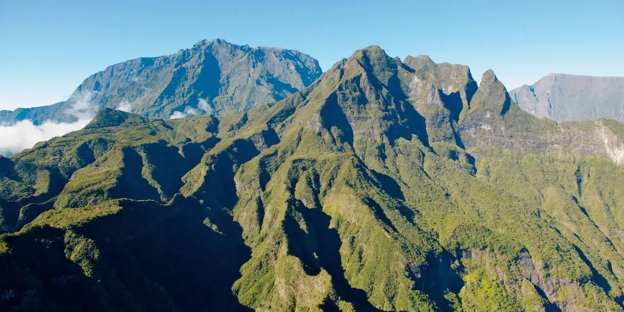Vastes montagnes verdoyantes sous un ciel bleu clair. Idéal pour planifier que faire à La Réunion, entre randonnées et panoramas.