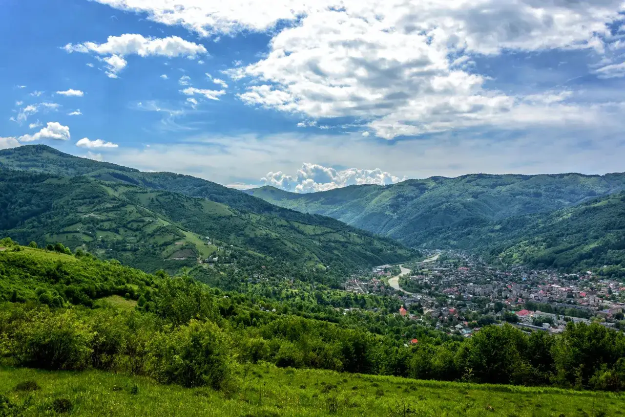 Zielone góry w Ukrainie, dolina z miasteczkiem i rzeką, błękitne niebo z chmurami.