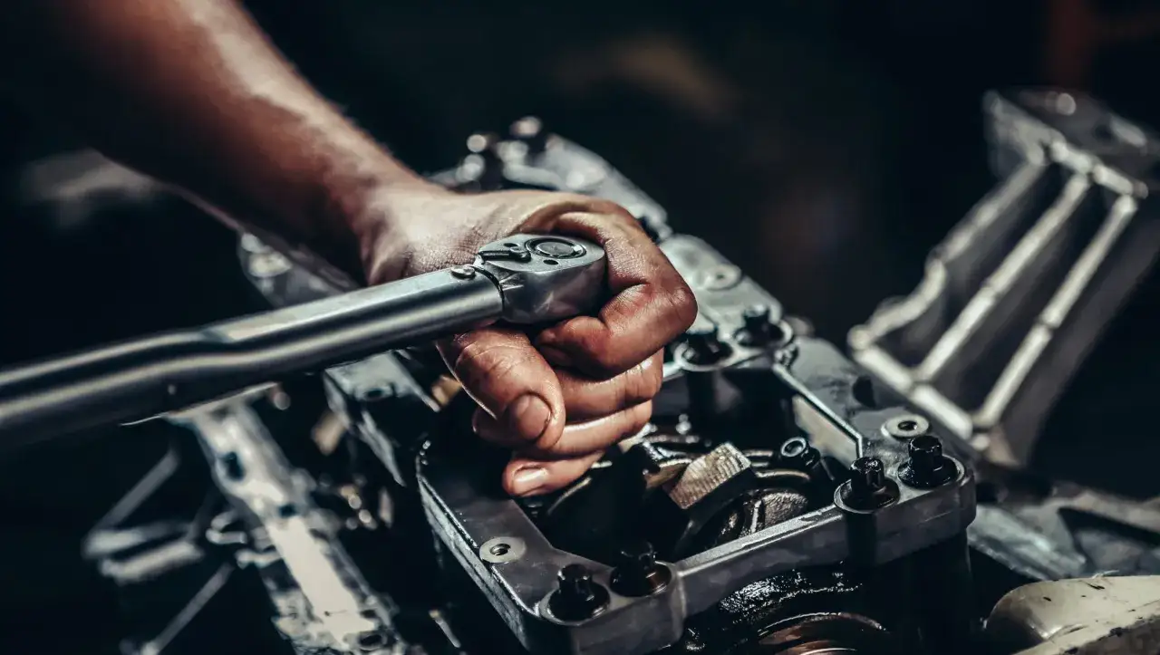 Mechanic's hand using a torque wrench on engine components, likely during a camshaft sensor replacement.