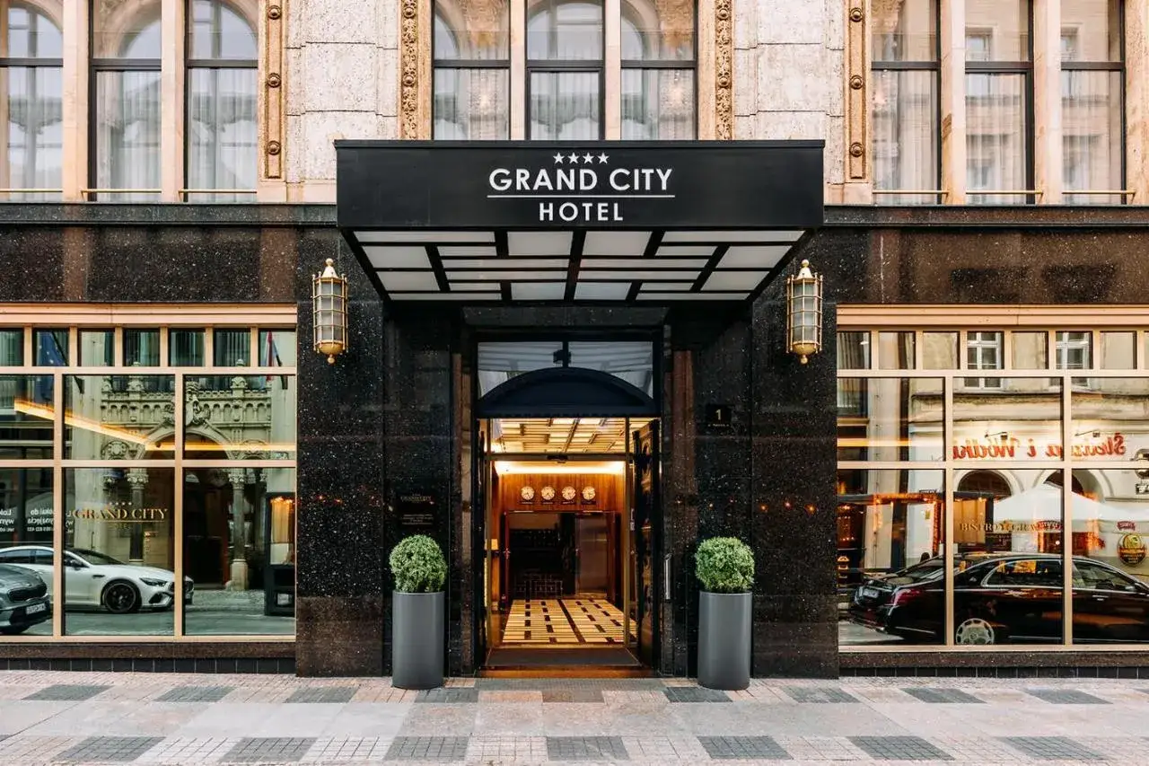 Elegancki **grand city hotel** z lśniącym wejściem, ozdobionym złotymi lampami i zielonymi roślinami.