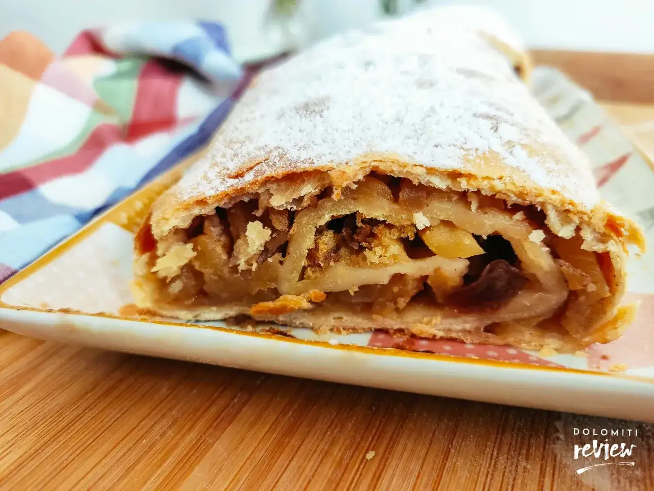 Strudel di mele con pasta sfoglia, cosparso di zucchero a velo, su un piatto decorato. Un dolce invitante, pronto per essere gustato.