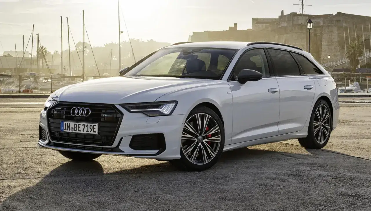 Białe Audi A6 Avant z napędem 50 TFSI co to za silnik? Eleganckie auto na tle portu z żaglówkami i zabytkową twierdzą.