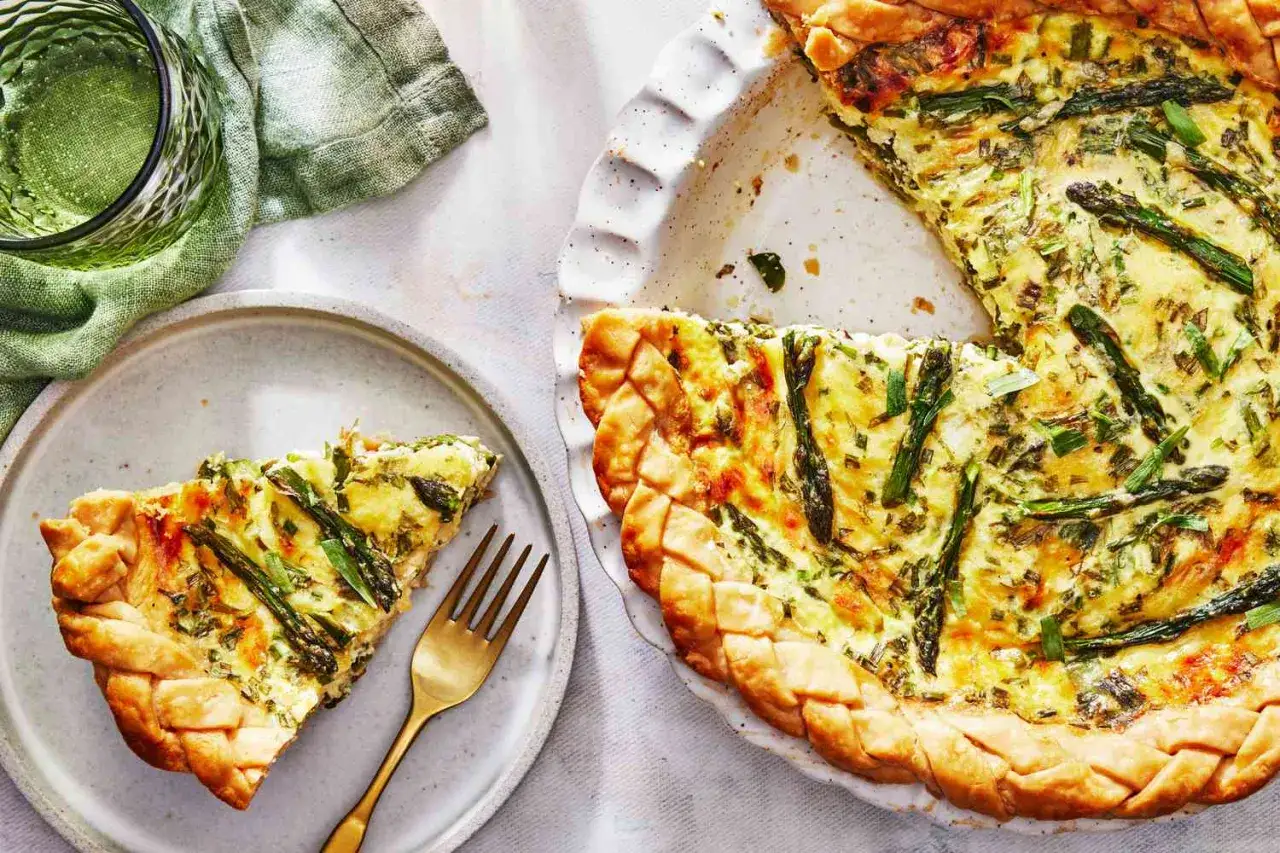 Herzhafte Spargel Quiche mit knusprigem Teigrand, ein St&uuml;ck auf einem Teller, daneben ein Glas Wasser.