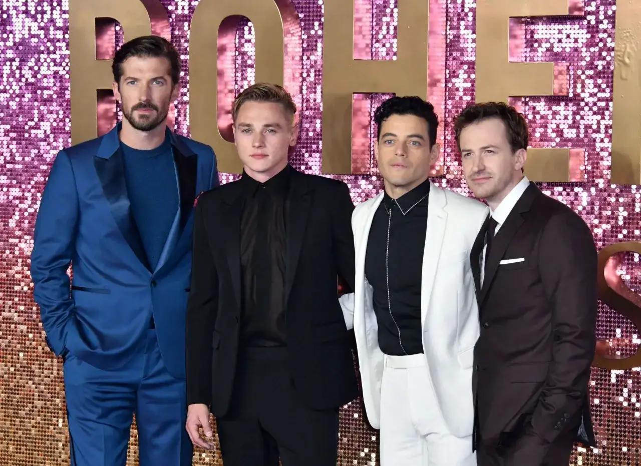 Aktorzy z filmu Bohemian Rhapsody: Rami Malek, Ben Hardy, Gwilym Lee i Joe Mazzello pozują na tle błyszczącej ścianki.