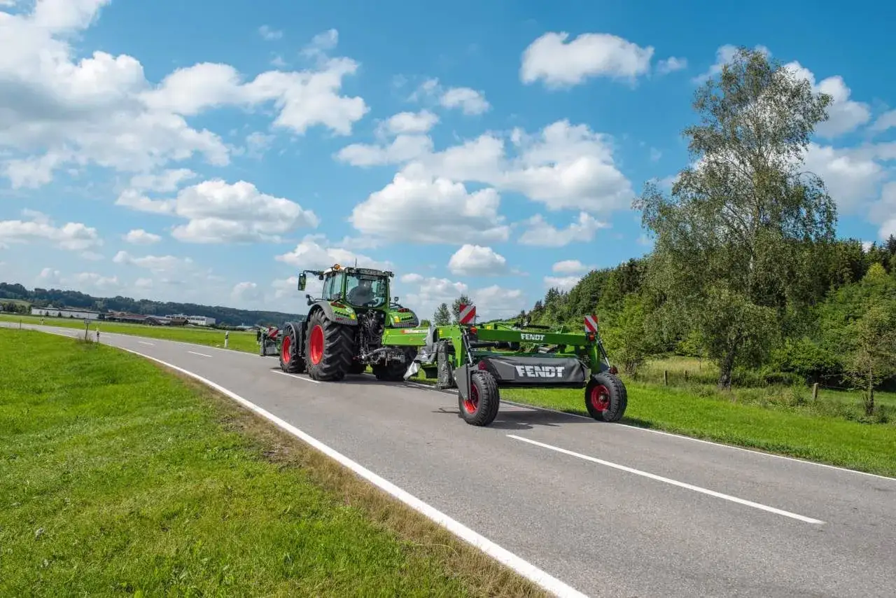 Trattore verde con falciatrice Fendt su strada extraurbana. Sulle autostrade e strade extraurbane principali è vietata la circolazione di macchine agricole.