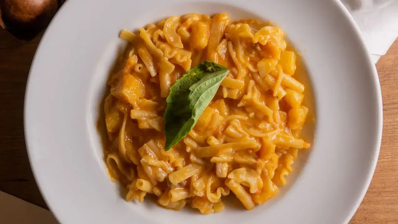 Un piatto di pasta con patate cremosa, arricchita da cubetti di patate e guarnita con una foglia di basilico fresco.