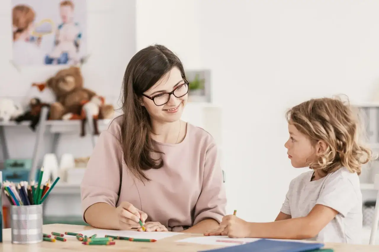 Uśmiechnięta terapeutka wspiera dziecko w procesie diagnozy ADHD, wspólnie rysując kredkami.