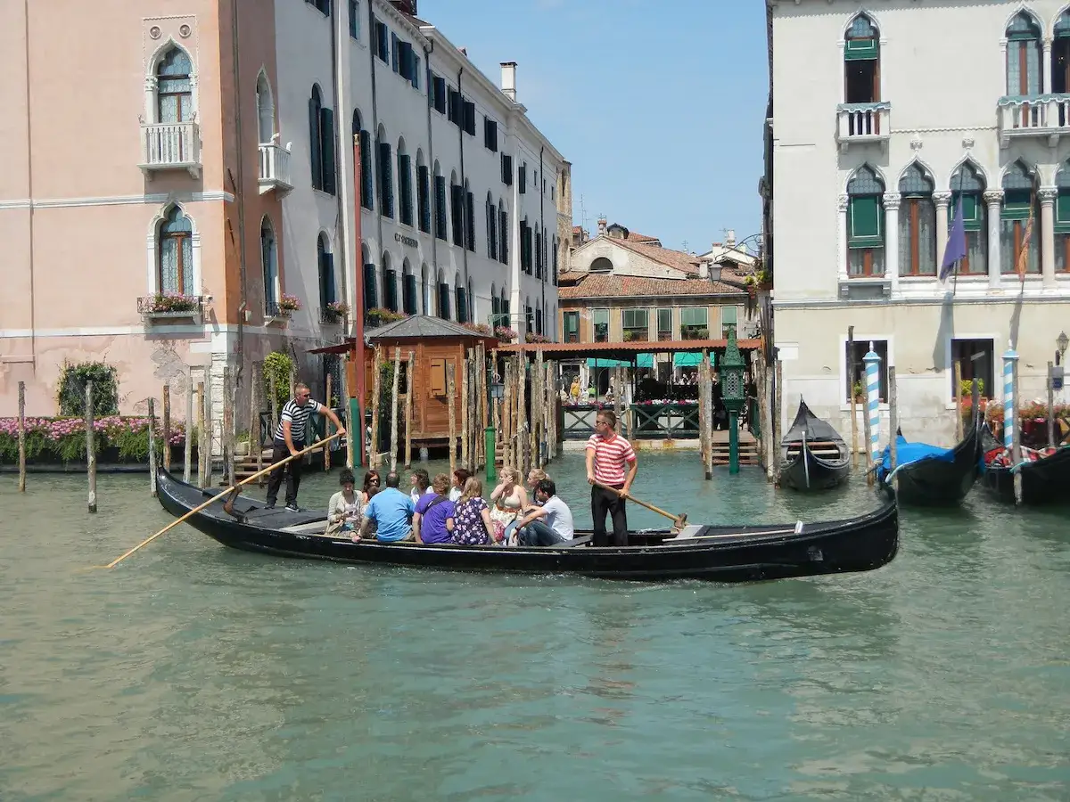 Gondola a Venezia con turisti e gondoliere, navigando tra palazzi storici e altri canali.