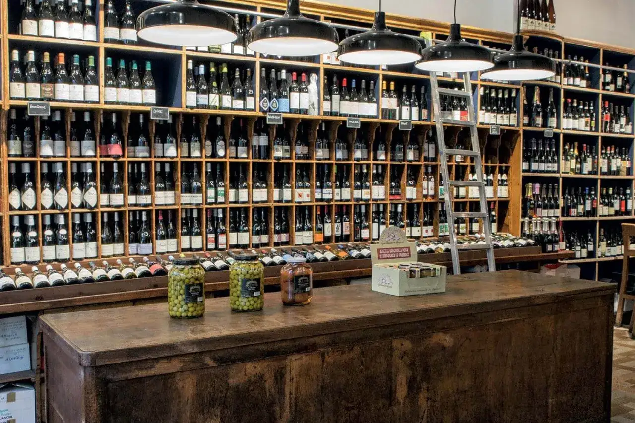 Étalages de bouteilles de vin, bocaux d'olives et de cornichons sur un comptoir en bois. Un paradis pour trouver le meilleur vin nature.