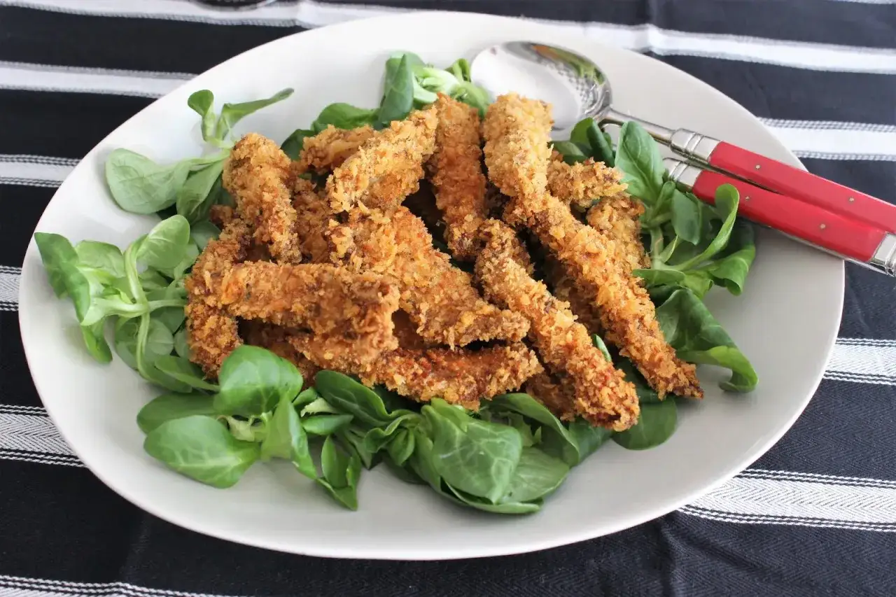 Crujientes tiras de pollo Popeye, perfectas para un bocado rápido en Zaragoza. Servidas sobre una cama de lechugas frescas.