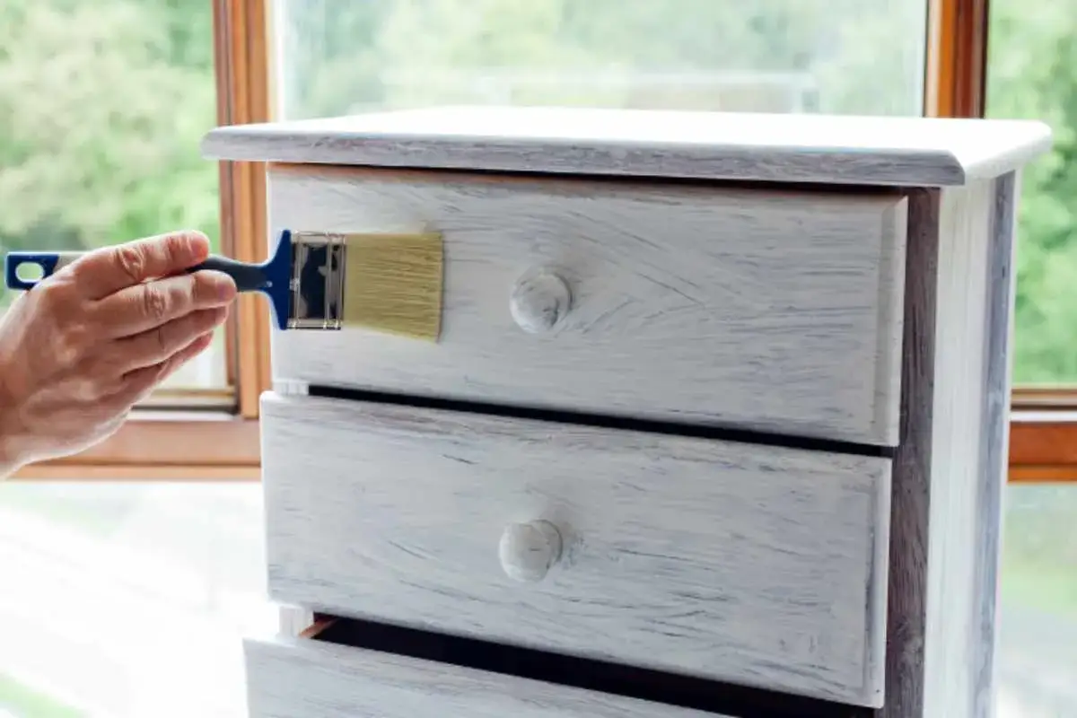 Mano che dipinge un cassettone con vernice a gesso, creando un effetto shabby chic.