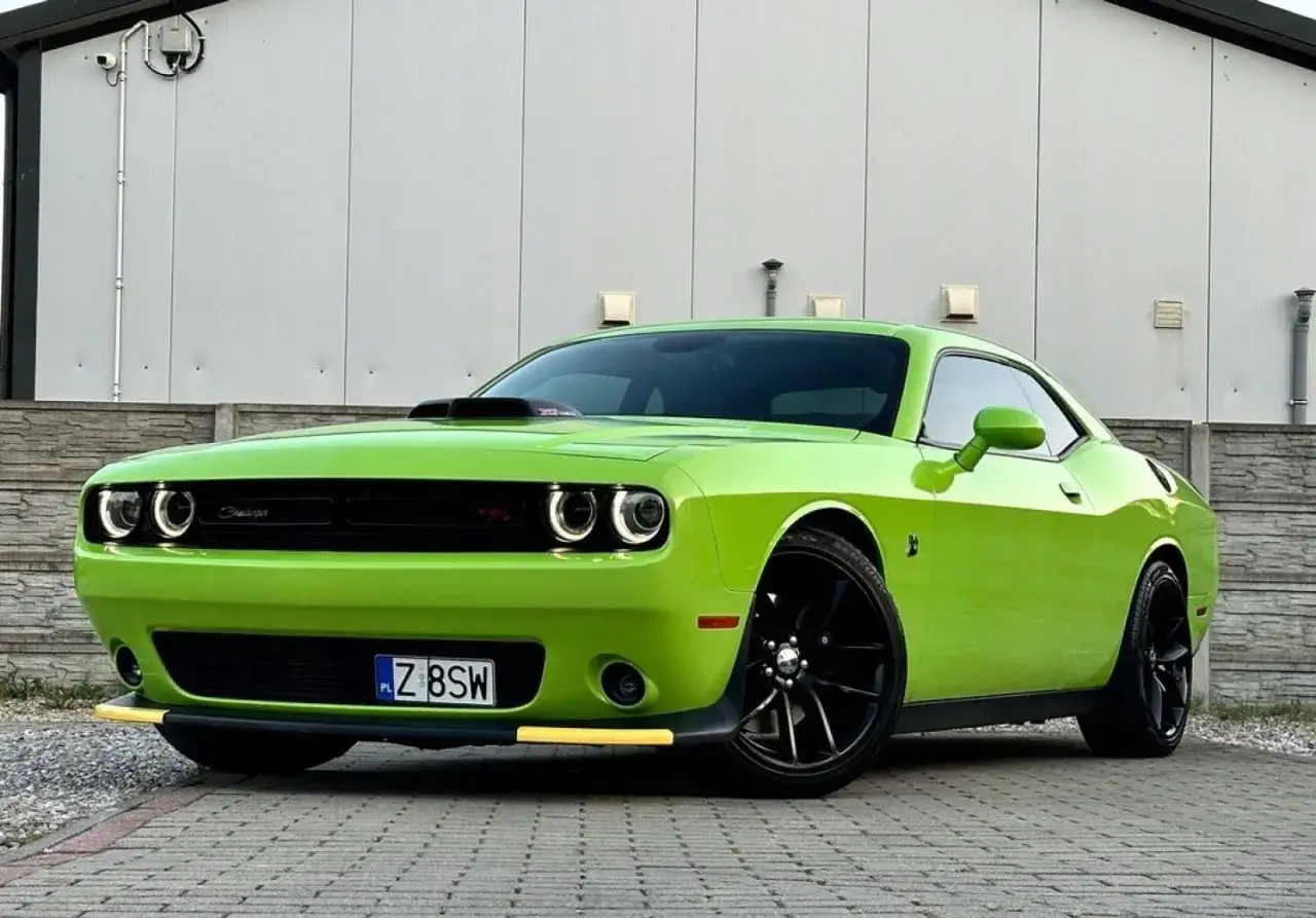 Jaskrawozielony Dodge Challenger SRT z czarnymi felgami i żółtym spoilerem prezentuje się imponująco na tle szarego budynku.