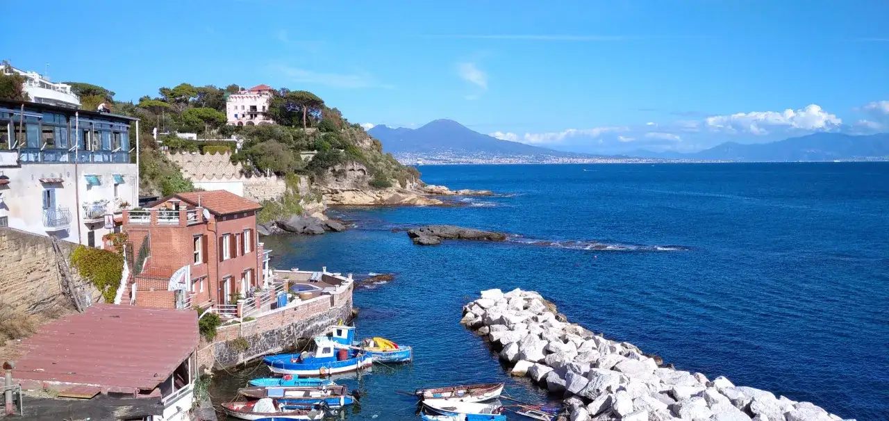 La fenestella di Marechiaro, con le sue case colorate e il mare blu, incornicia il Vesuvio in lontananza.