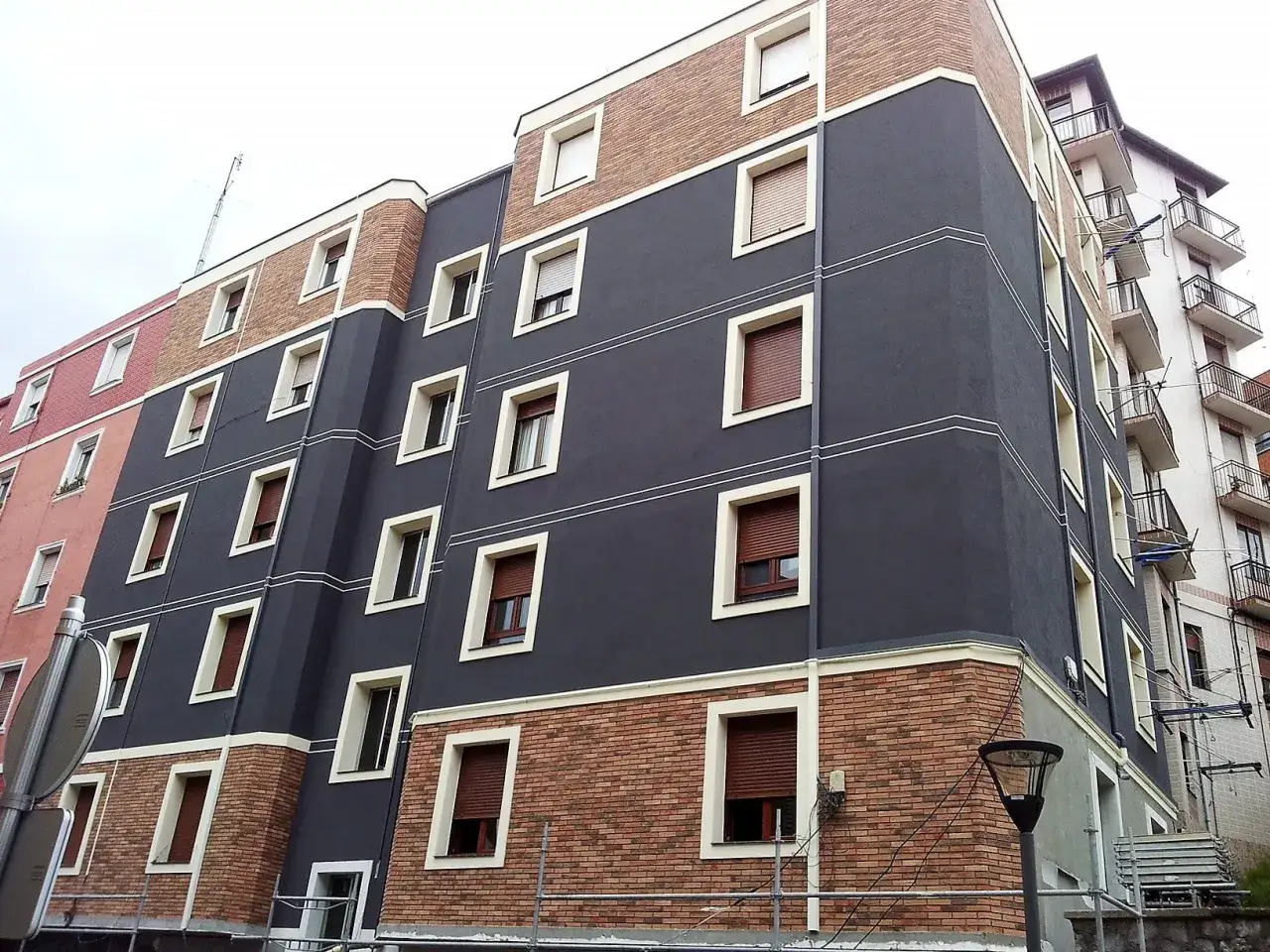 Edificio moderno con fachada de ladrillo y estuco gris, ventanas rectangulares y balcones. Un detalle sate sika en la esquina.