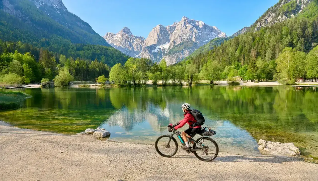 Ciclista en el Alpe Adria Radweg, junto a un lago alpino de aguas cristalinas y monta&ntilde;as imponentes.