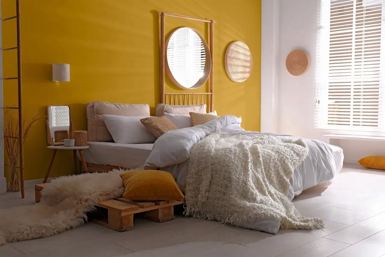 Chambre cosy avec mur jaune vif et blanc. Le lit est paré de draps blancs et d'une couverture texturée. Le jaune et le blanc sont 2 couleurs qui vont bien ensemble pour une chambre.