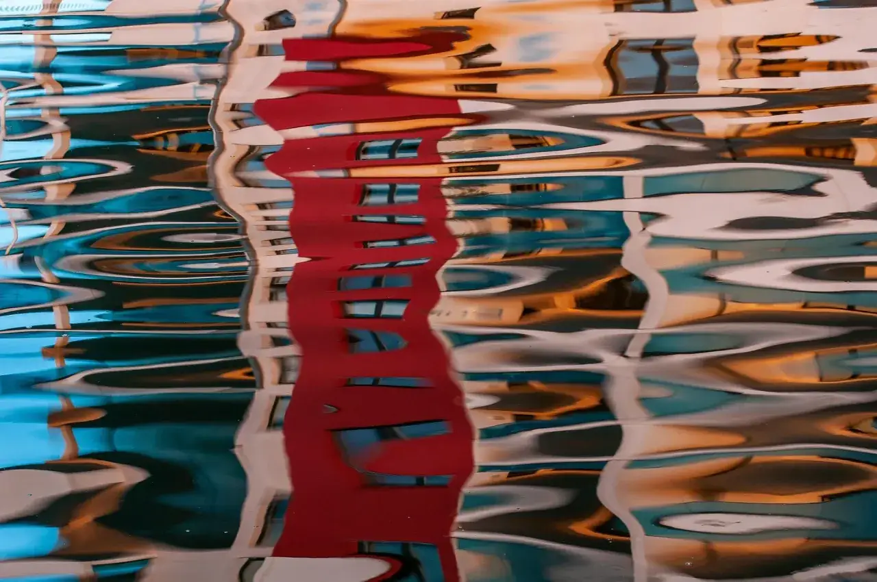 Reflets abstraits d'un bâtiment rouge et bleu sur l'eau. L'image montre comment peindre la transparence de l'eau avec des formes ondulées et des couleurs vives.