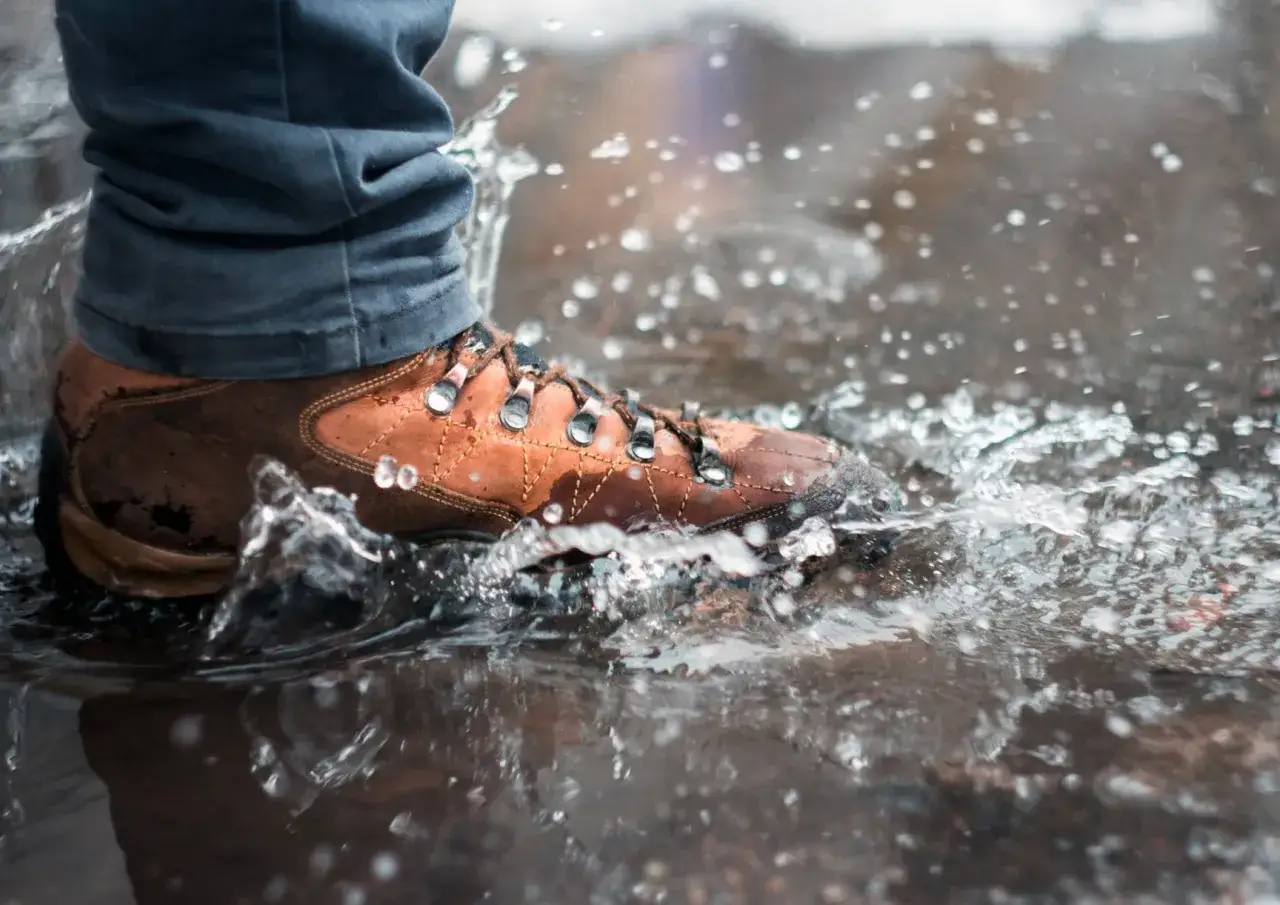 A brown hiking boot splashes through a puddle, a reminder that finding the best way to dry boots after such an adventure is crucial.