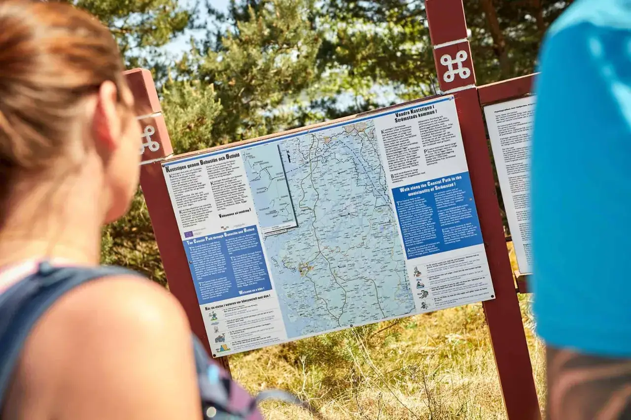 Kuststigen karta visar v&auml;gen l&auml;ngs Bohusl&auml;ns vackra kust. Tv&aring; personer studerar kartan innan vandringen.