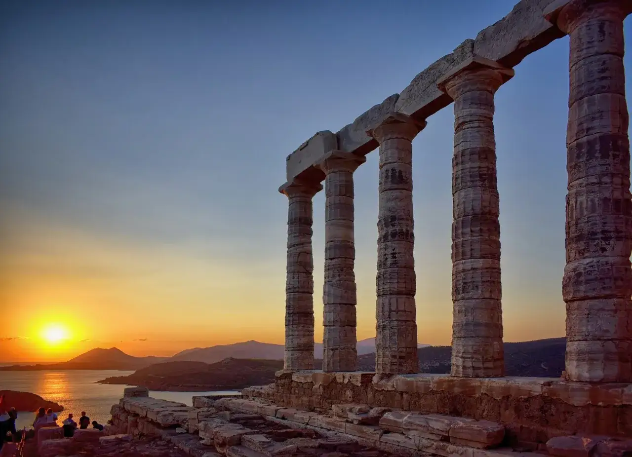 Antiche colonne del Tempio di Poseidone a Capo Sounion, illuminate dal tramonto dorato sul mare Egeo.