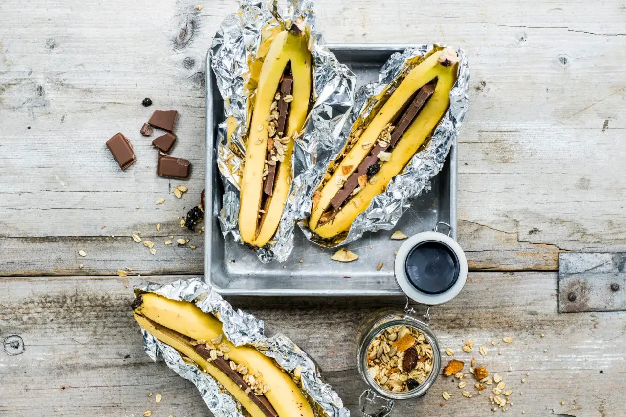 Banane al cioccolato e muesli, pronte per essere cotte, su un vassoio metallico e su un tavolo di legno grezzo.