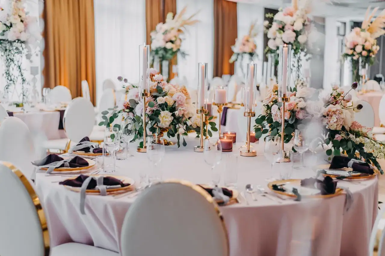 Eleganckie nakrycia stoł&oacute;w z pastelowymi kwiatami i złotymi świecznikami. Wspaniałe pomysły na wesele w romantycznym stylu.