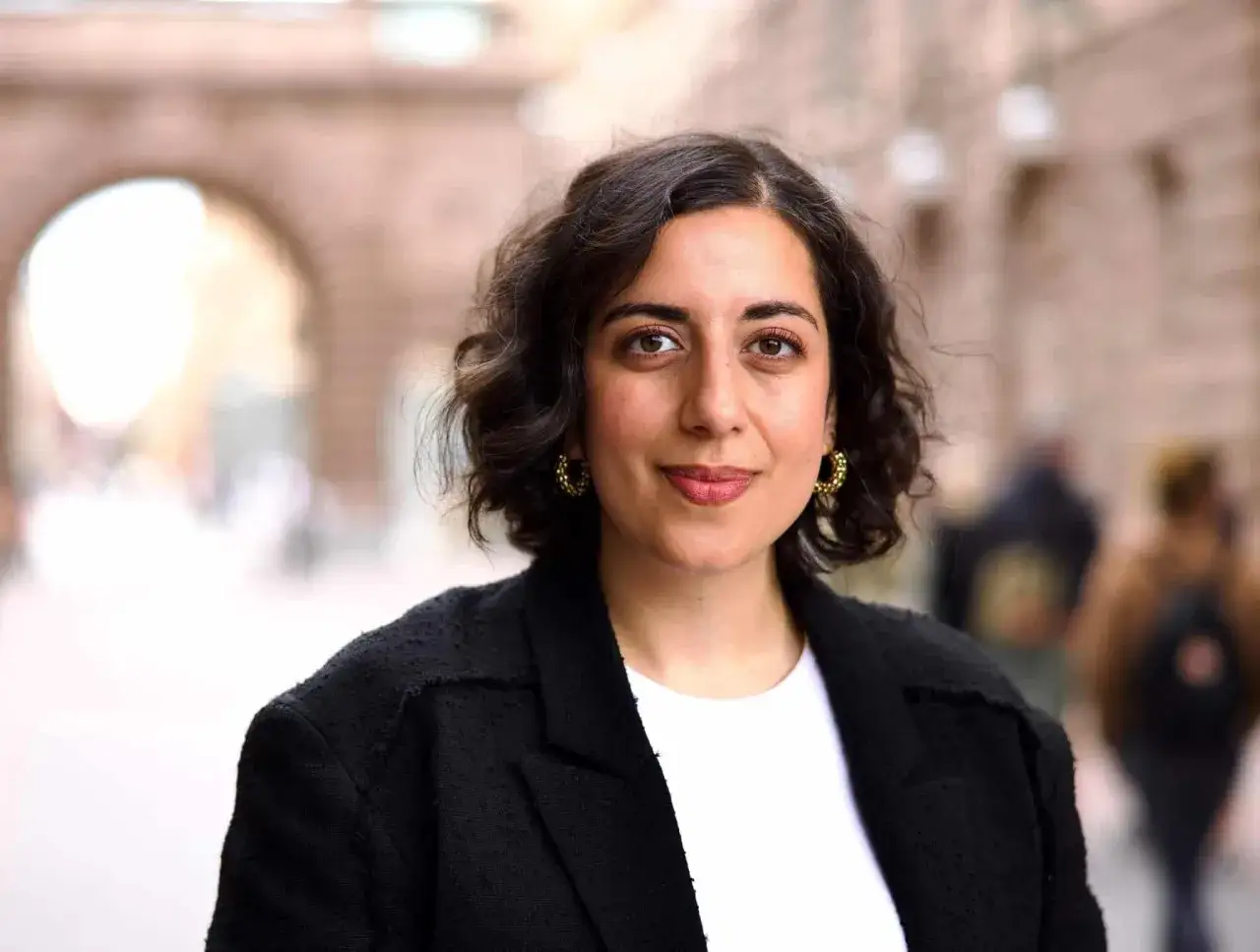 En kvinna med m&ouml;rkt lockigt h&aring;r och stora &ouml;rh&auml;ngen, kl&auml;dd i en svart kavaj, poserar utomhus. Hon ser ut som en framst&aring;ende person, kanske folkpartiet partiledare.