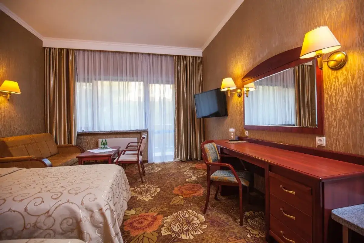 Pokój hotelowy z łóżkiem, kanapą, biurkiem i oknem. Zastanawiasz się, ile kosztuje doba w hotelu Gołębiewski dla dwóch osób?