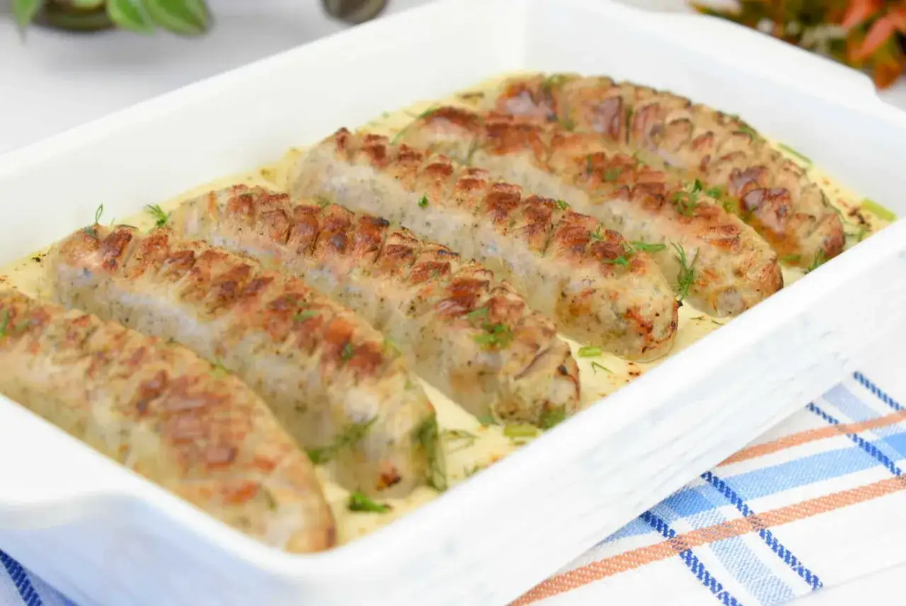 Aromaticzna biała kiełbasa w sosie chrzanowo-musztardowym, posypana świeżym koperkiem, prezentuje się apetycznie w białej zapiekance.