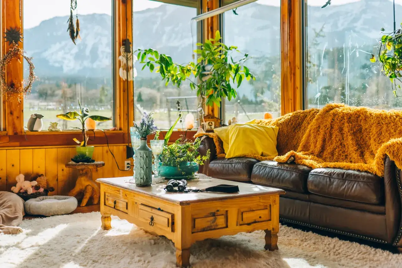 Un accogliente soggiorno con vista sulle montagne, un divano in pelle marrone con coperta arancione e un tavolino in legno. Questa casa super moderna &egrave; piena di piante e decorazioni boh&eacute;mien.